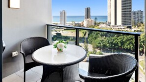 A balcony with a round table and two wicker chairs, overlooking a cityscape with tall buildings and a clear sky. - Chic 1BR Getaway Steps from Beach&Surfers Paradise (Surfers Paradise)