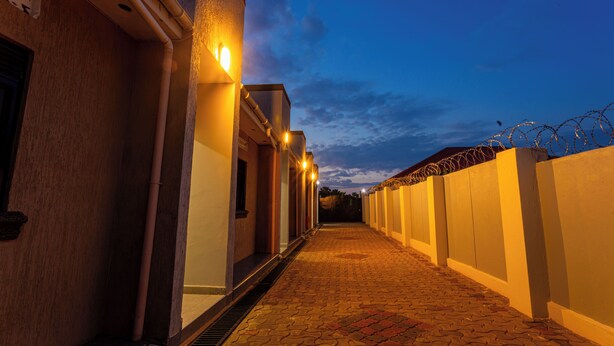 Un chemin pavé mène à un bâtiment dont l’extérieur est illuminé et qui est protégé par une clôture de sécurité surmontée de barbelés.