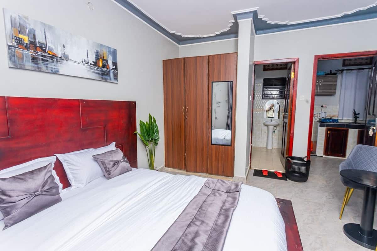 A hotel room with a large bed, a wardrobe, a bathroom, and a small seating area.