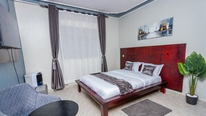 Une chambre d’hôtel avec un lit, une chaise, une petite table, une plante en pot et un tableau au mur.