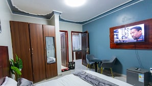Une chambre d’hôtel comprenant un lit, un téléviseur fixé au mur, un bureau avec une chaise et une armoire.
