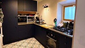 A compact kitchen with dark cabinets, a gas stove, a microwave, and a patterned floor. - The Babouz Cottage, 4*,  entire house in the heart of Mirepoix and Cathars area (Mirepoix)