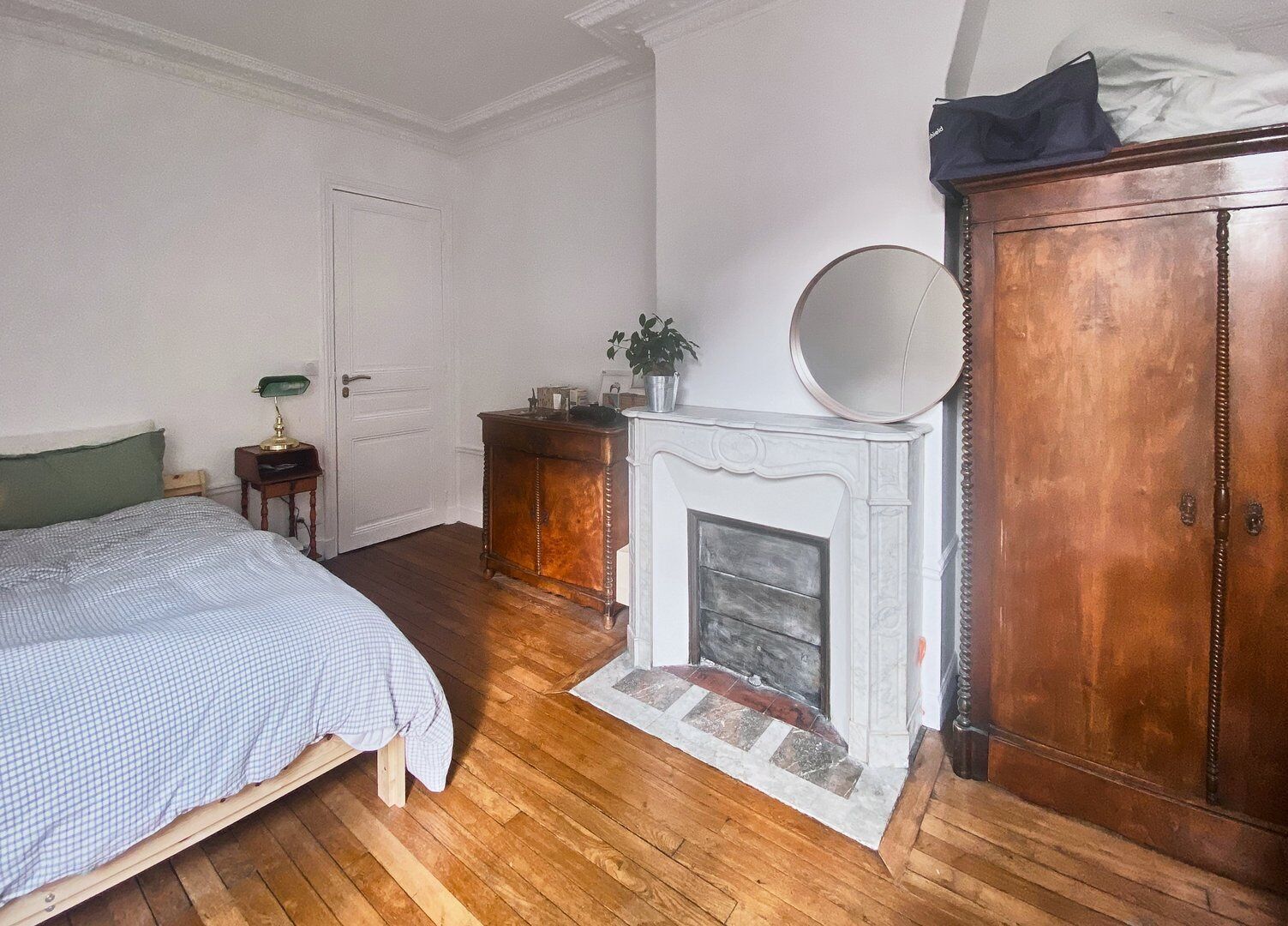 A bedroom with a bed, a nightstand, a dresser, a mirror, and a fireplace.