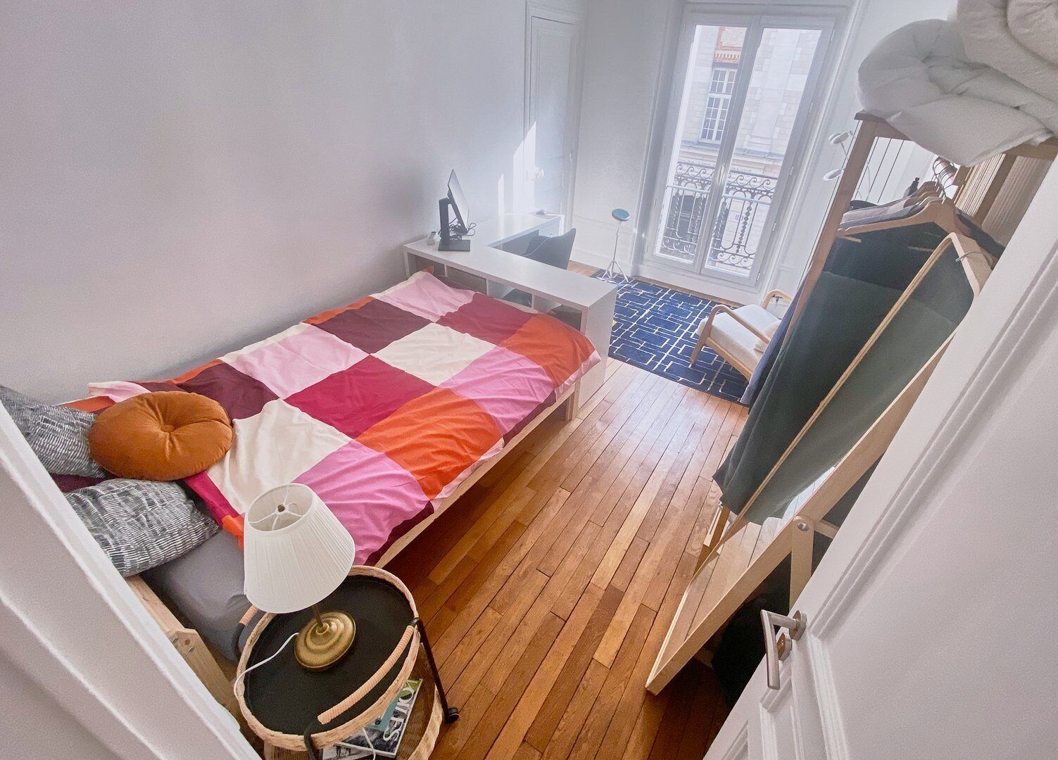 Habitación compacta con cama, mesita de noche, lámpara y un ventanal pequeño.