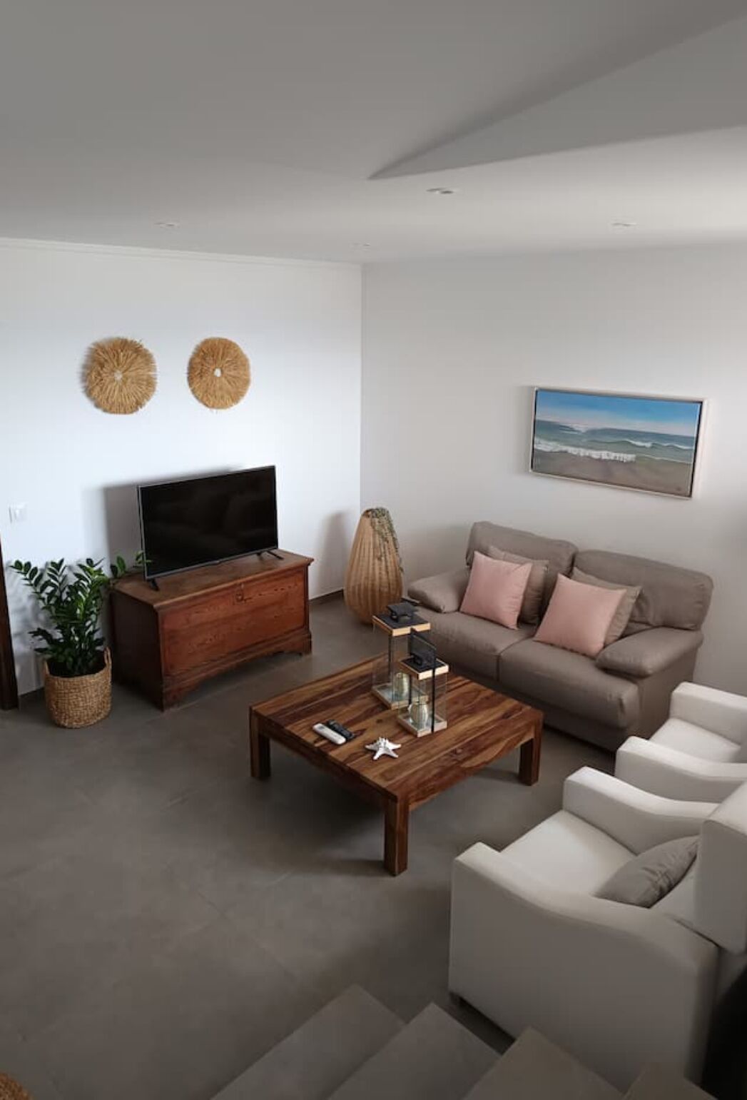 Ett modernt vardagsrum med en platt-TV, ett soffbord i trä, en beige soffa och en vit fåtölj.