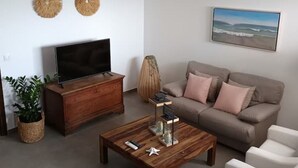 Un salon moderne avec un téléviseur à écran plat, une table basse en bois, un canapé beige et un fauteuil blanc.