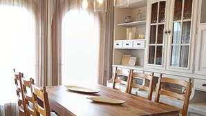 Un coin repas avec une table et des chaises en bois, des luminaires suspendus et un meuble avec des portes en verre.