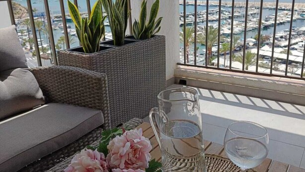 Un balcon agrémenté de meubles en osier, d’une plante en pot, d’une carafe d’eau et d’un verre d’eau posés sur un set de table en fibres tressées.