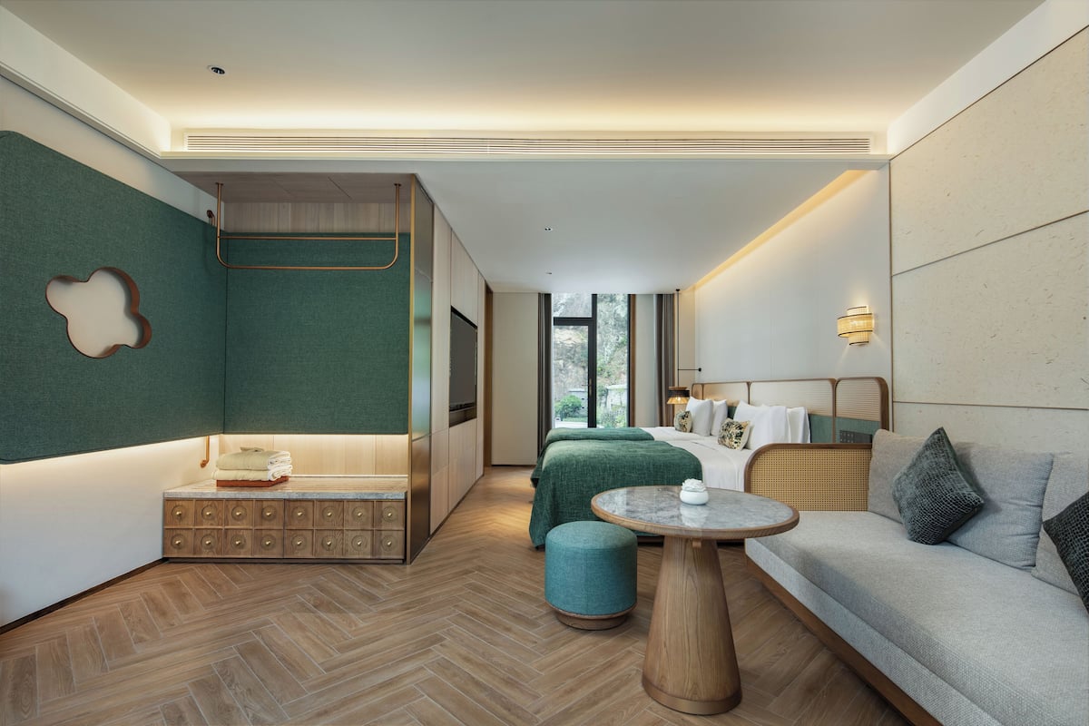 A modern hotel room with a bed, a sofa, a small table, and a TV.