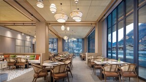 A modern dining area with high ceilings, large windows, and a view of mountains.