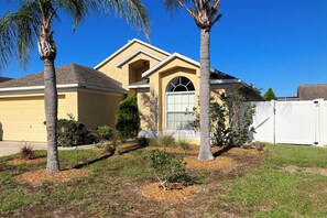 Une maison d’habitation avec un garage, une allée et une pelouse bien entretenue agrémentée de palmiers.