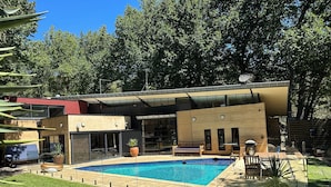 Ein moderner Außenpoolbereich mit einem rechteckigen Pool, umgeben von einer Holzterrasse und Topfpflanzen.