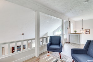 Ein großzügiger Wohnbereich mit hoher Decke und Balkon. Zwei blaue Sessel und ein Couchtisch mit Dekorationselementen.