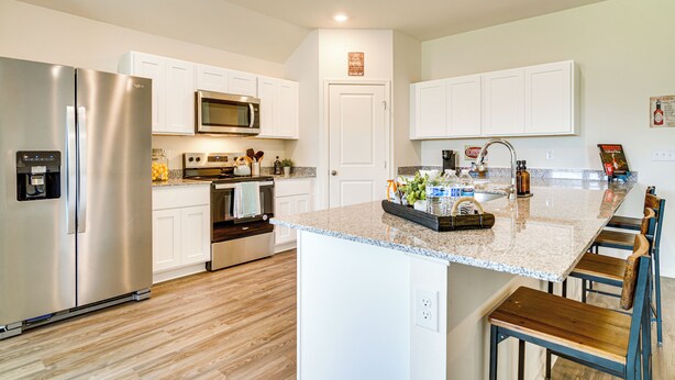 Una cocina moderna con armarios blancos, electrodomésticos de acero inoxidable, encimera de granito y taburetes de bar de madera.