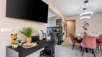 Una cocina moderna con un televisor de pantalla plana, un comedor con sillas rosadas y una zona de bar con encimera negra.