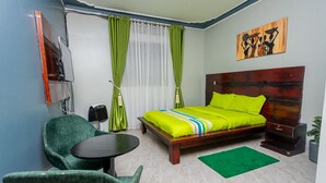A bedroom with a bed, green chairs, a small table, a bedside table, and a painting on the wall. - The Den Soroti Green (Soroti)