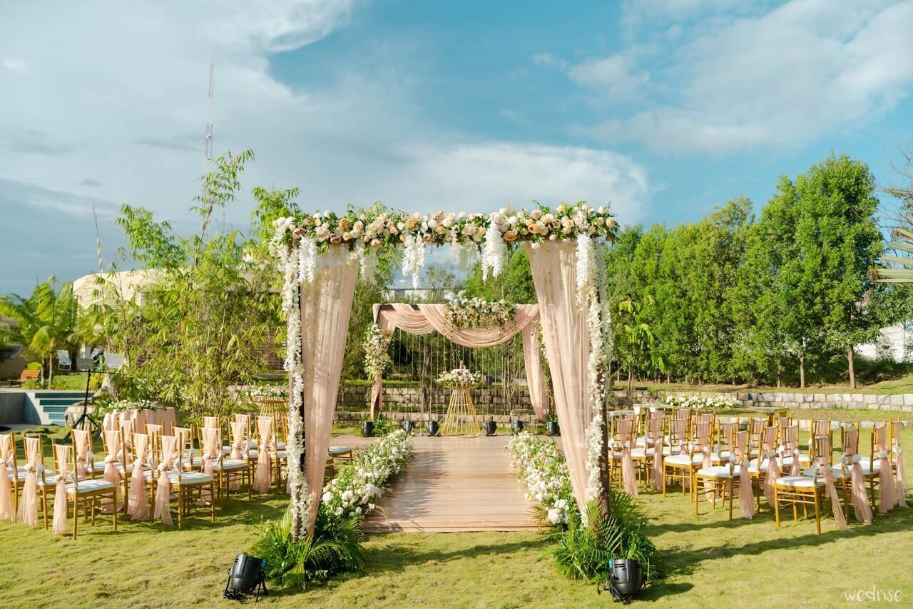 Eine Hochzeitslocation im Freien mit einem hölzernen Gang, floralen Dekorationen und Reihen von Stühlen.