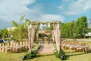 An outdoor wedding venue with a wooden aisle, floral decorations, and rows of chairs. - ELIVAAS Urvi Resort | Eco-Luxury Getaway with Pool (Chikkellur)
