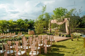 An outdoor wedding venue with rows of wooden chairs, a stage with draped fabric, and lush greenery. - ELIVAAS Urvi Resort | Eco-Luxury Getaway with Pool (Chikkellur)