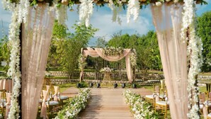 An outdoor wedding venue with a wooden aisle, floral arches, and seating arrangements. - ELIVAAS Urvi Resort | Eco-Luxury Getaway with Pool (Chikkellur)