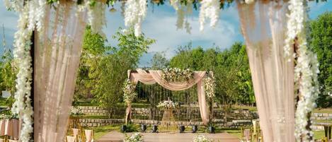 An outdoor wedding venue with a wooden aisle, floral arches, and seating arrangements.