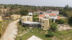 A residential area with multiple houses, a paved pathway, and a small garden area. - ELIVAAS Urvi Resort | Eco-Luxury Getaway with Pool (Chikkellur)