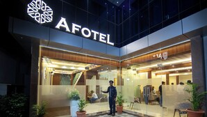 The exterior of an AFOTEL with a modern design, featuring a glass facade, a security guard, and potted plants. - Hotel Afotel Mumbai-Near International Airport (Mumbai)