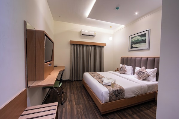 A hotel room with a bed, a desk, a chair, a TV, and an air conditioner.