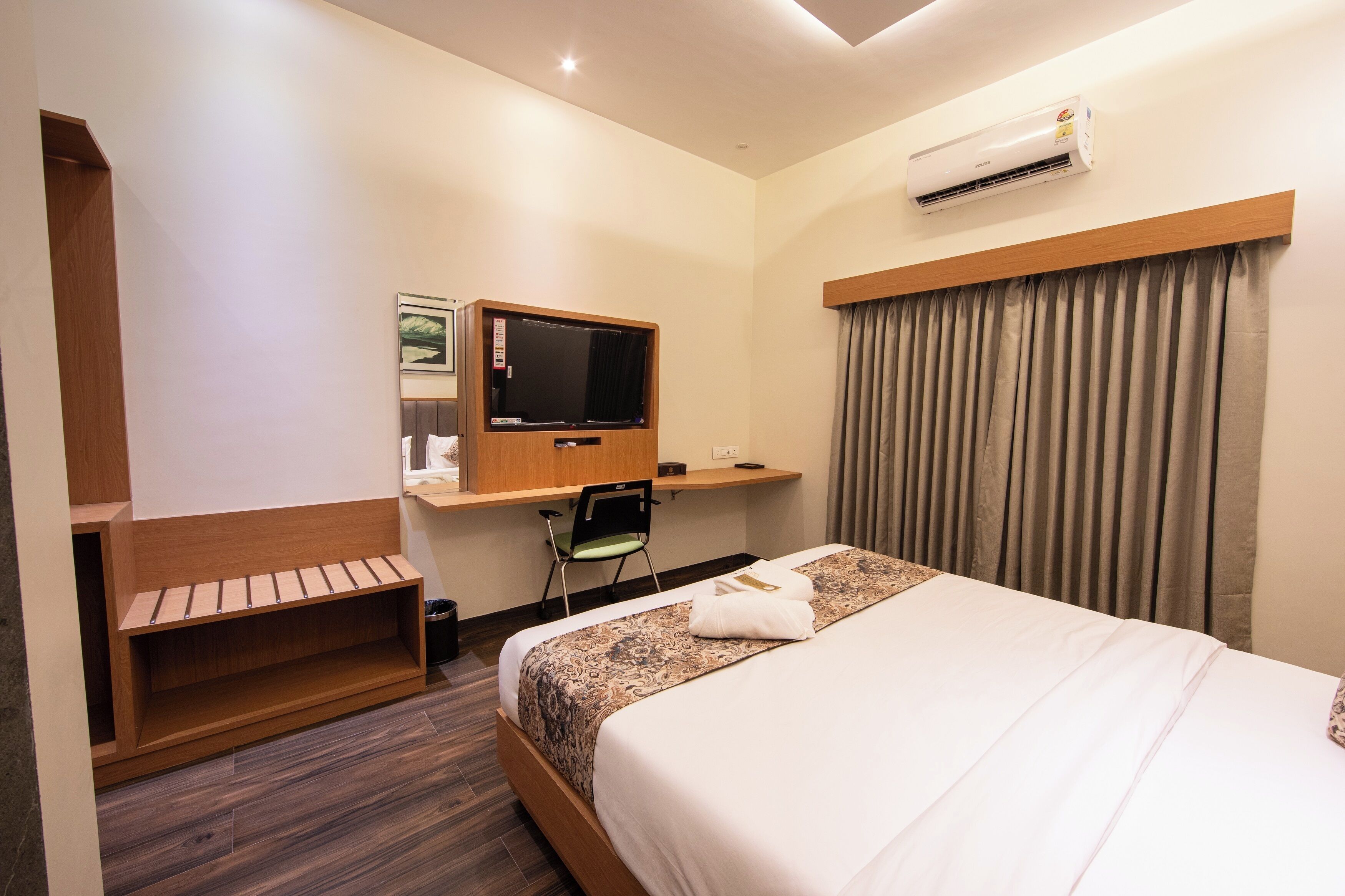 Habitación de hotel con cama, escritorio con televisor, una silla y estantería empotrada.