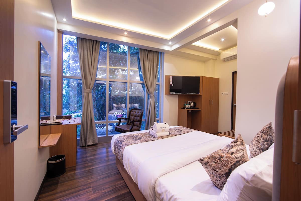 A modern hotel room with a large bed, a desk, a chair, and a TV.