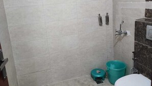 A small bathroom with a shower, toilet, and a bucket. - JN RESIDENCY (Gurugram)