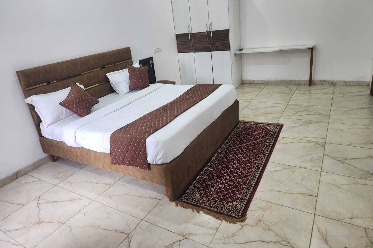 A bedroom with a bed, pillows, a bedside table, a wardrobe, and a patterned rug.