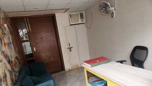 A room with a blue chair, a yellow desk with books, a door, and an air conditioning unit. - JN RESIDENCY (Gurugram)