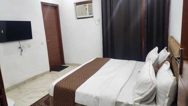 A bedroom with a bed, a television mounted on the wall, a door, and an air conditioning unit. - JN RESIDENCY (Gurugram)