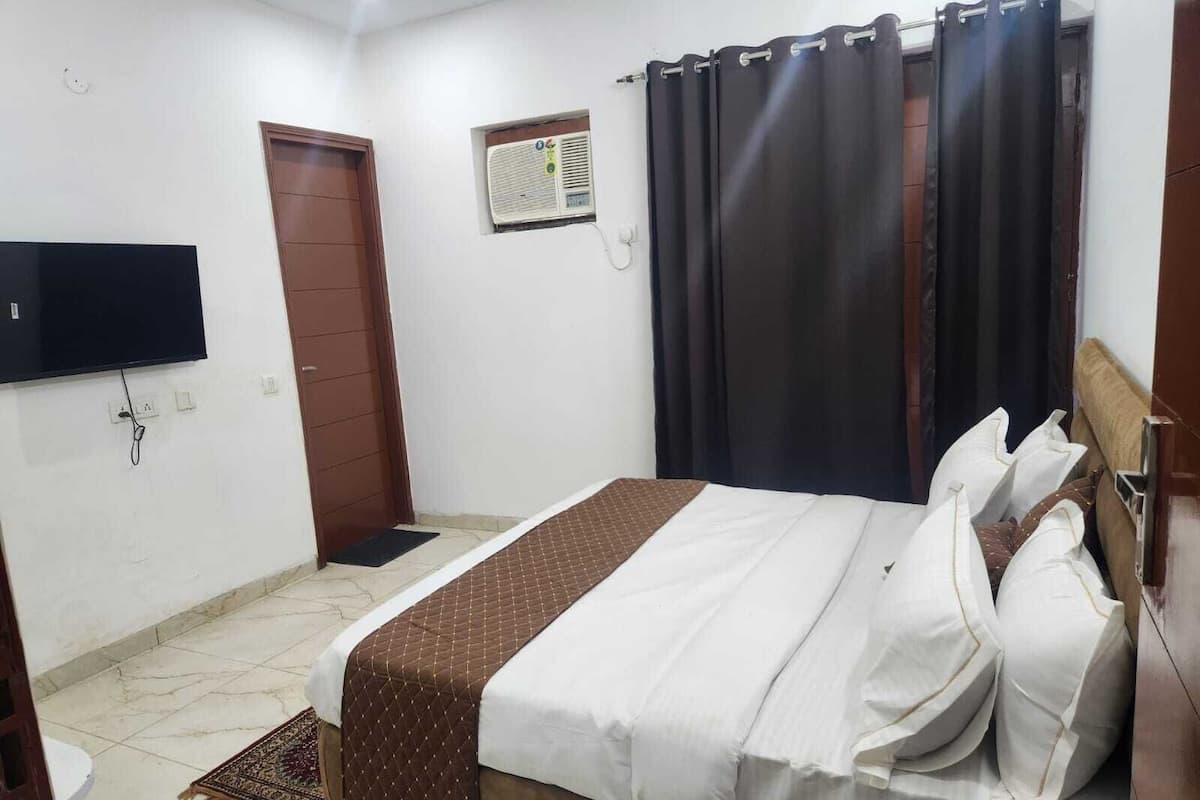 A bedroom with a bed, a television mounted on the wall, a door, and an air conditioning unit.