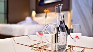 A hotel room with a bed, a bedside table with a bottle and glasses, and a flower on the table.