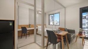 A modern hotel room with a kitchenette, a dining area, a bed, and a large window offering a city view. - TCM Hotel & Apartment (Da Nang)