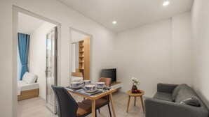 A modern living room with a dining area, a grey sofa, a TV, and a small side table with decorative items. - TCM Hotel & Apartment (Da Nang)