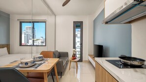 A modern hotel room with a dining area, a sofa, a TV, and a view of the city. - TCM Hotel & Apartment (Da Nang)