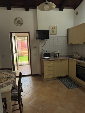 A kitchen with a microwave, stove, and sink. There is a door leading to a patio. - Sa Domu Arrosada Close to the most beautiful beaches, out of the chaos (Solarussa)