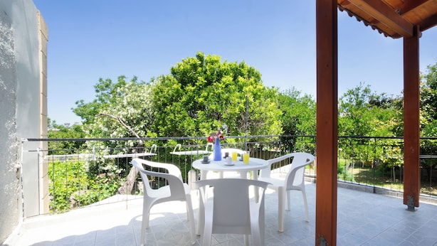 A covered outdoor seating area with a table and chairs, a view of greenery, and a clear sky. - Galatas Maisonette (Galatas)