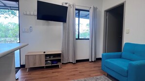 Ein Wohnzimmer mit einem blauen Sofa, einem an der Wand montierten Fernseher, einem kleinen Holzschrank und einem gemusterten Teppich.