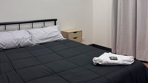 Ein Schlafzimmer mit einem schwarzen Bett, weißen Kissen, einem hölzernen Nachttisch und einer weißen Klimaanlage an der Wand.