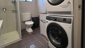 Ein Waschraum mit einer Waschmaschine und einem Trockner, einer Toilette und einer Duschgelegenheit.