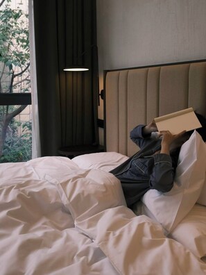 Une personne allongée sur un lit dans une chambre d’hôtel, en train de lire un livre.