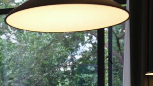 A bed with white linens and a person lying down, a large window with a view of greenery, and a hanging lamp above the bed. - Ayata Hotel (Chengdu)
