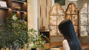 A woman reading a magazine at a wooden counter with a potted plant and a decorative screen in the background. - Ayata Hotel (Chengdu)