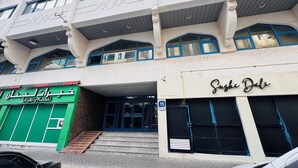 Un immeuble à plusieurs étages, avec une devanture verte au rez-de-chaussée et un restaurant de sushis au deuxième étage.