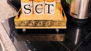 Un plan de travail de cuisine avec un plateau contenant des récipients étiquetés pour le sucre, le café et le thé, une machine à café, une bouilloire et une plante.