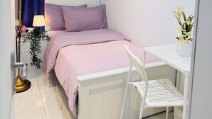 Une chambre à coucher comprenant un lit, une table de chevet, une chaise, une lampe, des rideaux et une plante en pot.